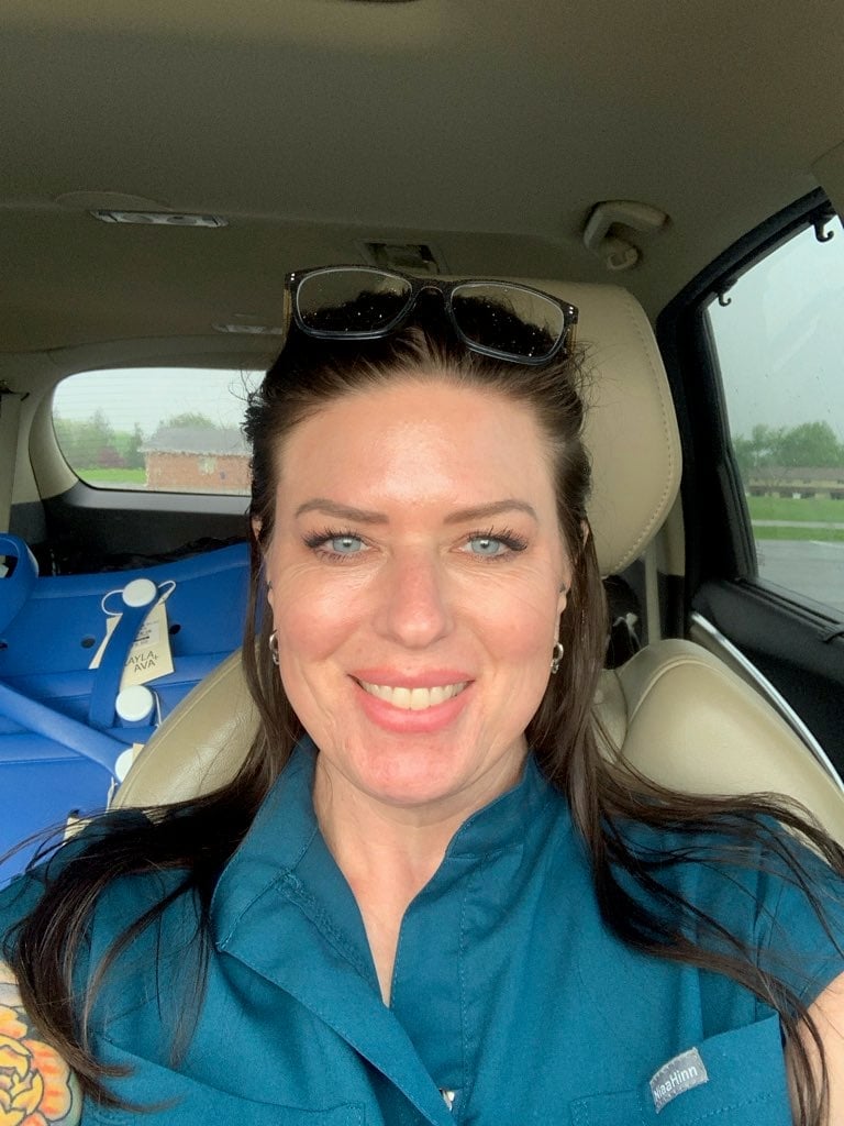 Woman with sunglasses on head wearing blue shirt, smiling in car interior with beige seats