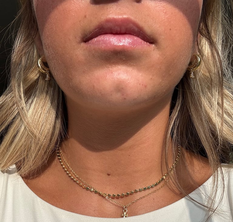 Close-up portrait of a woman with long wavy blonde hair, wearing a white shirt and gold chain necklace